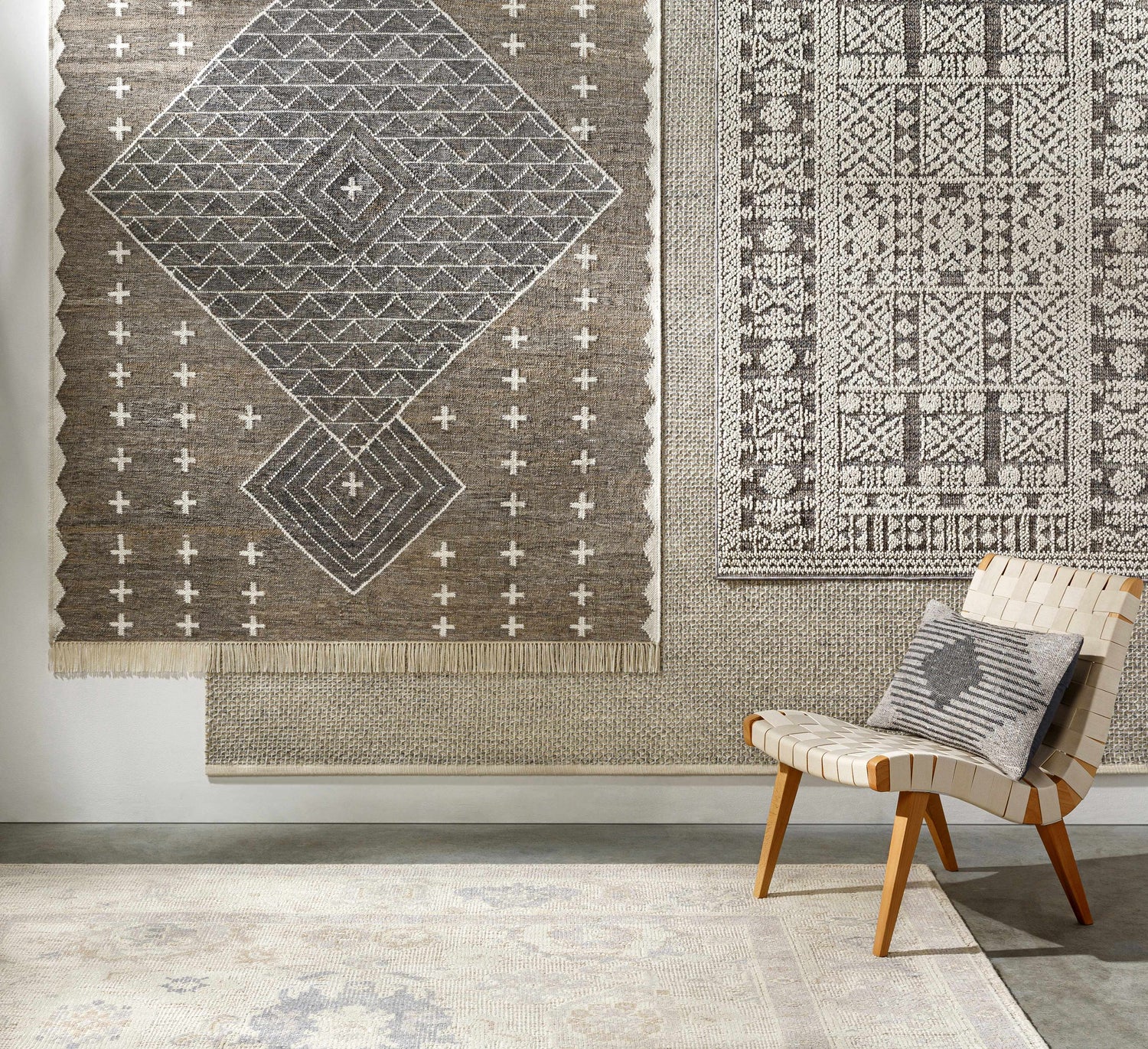Room scene with charcoal and cream Lodwar Area Rugs on the wall and floor, styled with a woven chair. Styleshot