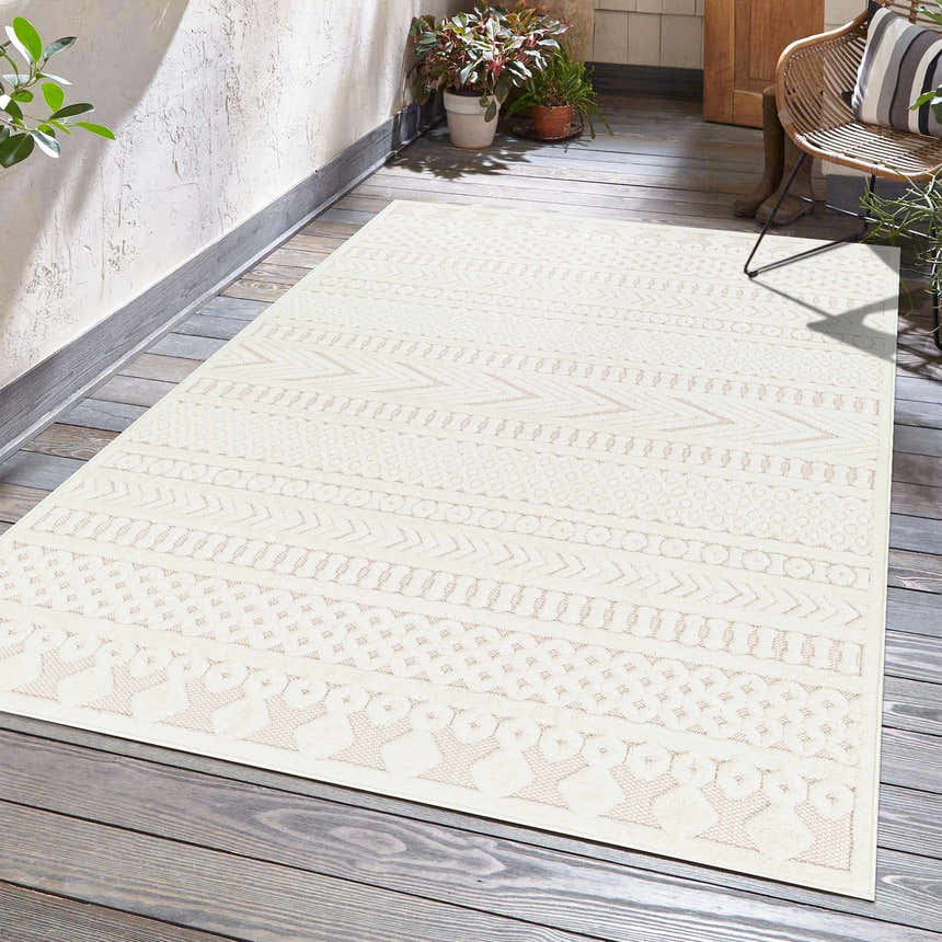 Patio scene with a cream Southwestern style Jove Cream Outdoor Rug, wicker chair, plants, and wood floor. Roomscene-Rectangle