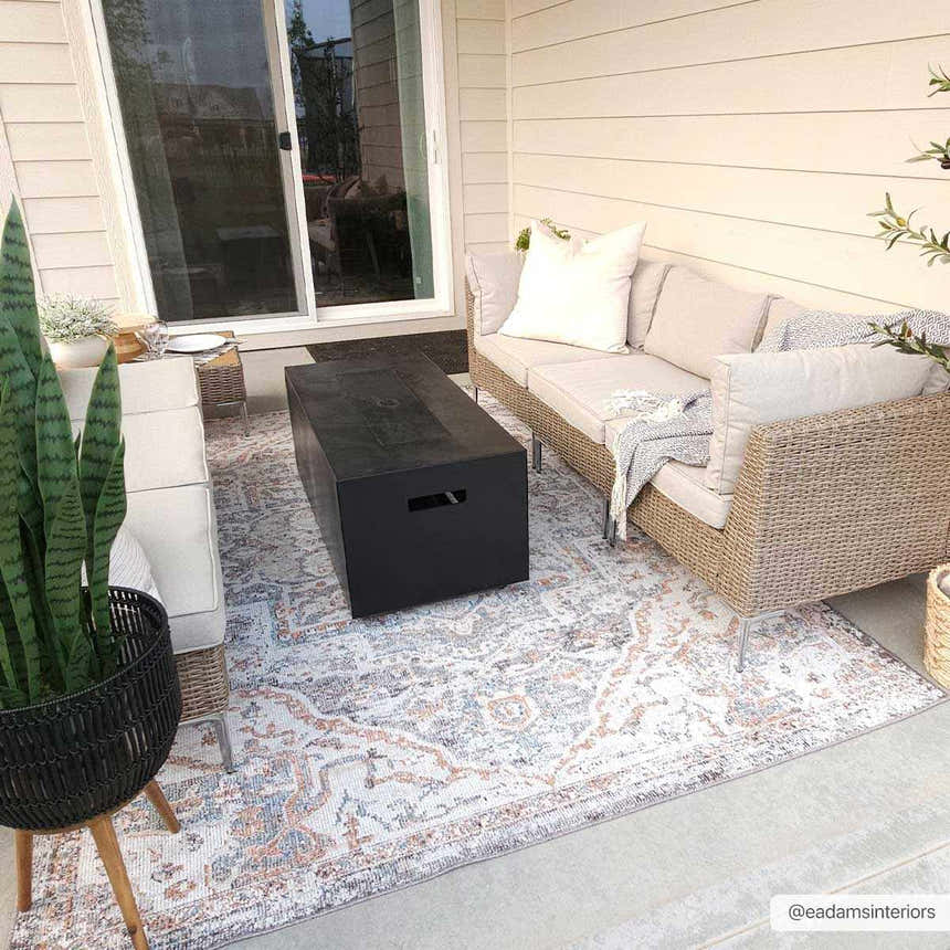 Outdoor patio scene with a beige sofa, black fire pit, and Tongala Indoor & Outdoor Rug in beige, blue, and brick red. Roomscene-Rectangle