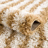 Close-up of the Calup Shag Area Rug showing its bone and dark brown striped pattern and plush, shaggy texture. Fold