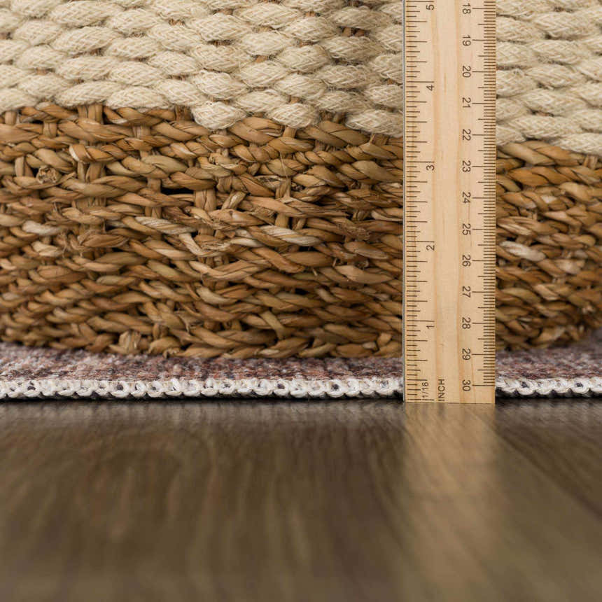 Close-up of the Ohoud Washable Area Rug showing its low pile, neutral colors, and woven edge detail with a measuring ruler. Pile