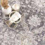Close-up of the Mohan Washable Area Rug with a traditional pattern in gray, beige, and white tones. Vases are styled on the rug. Styleshot