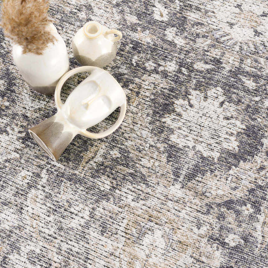 Close-up of the Mohan Washable Area Rug with a traditional pattern in gray, beige, and white tones. Vases are styled on the rug. Styleshot