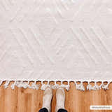 Close-up of the bone-colored Vineyards 3D Living Room Rug with geometric pattern and fringe on wood floor. Pile