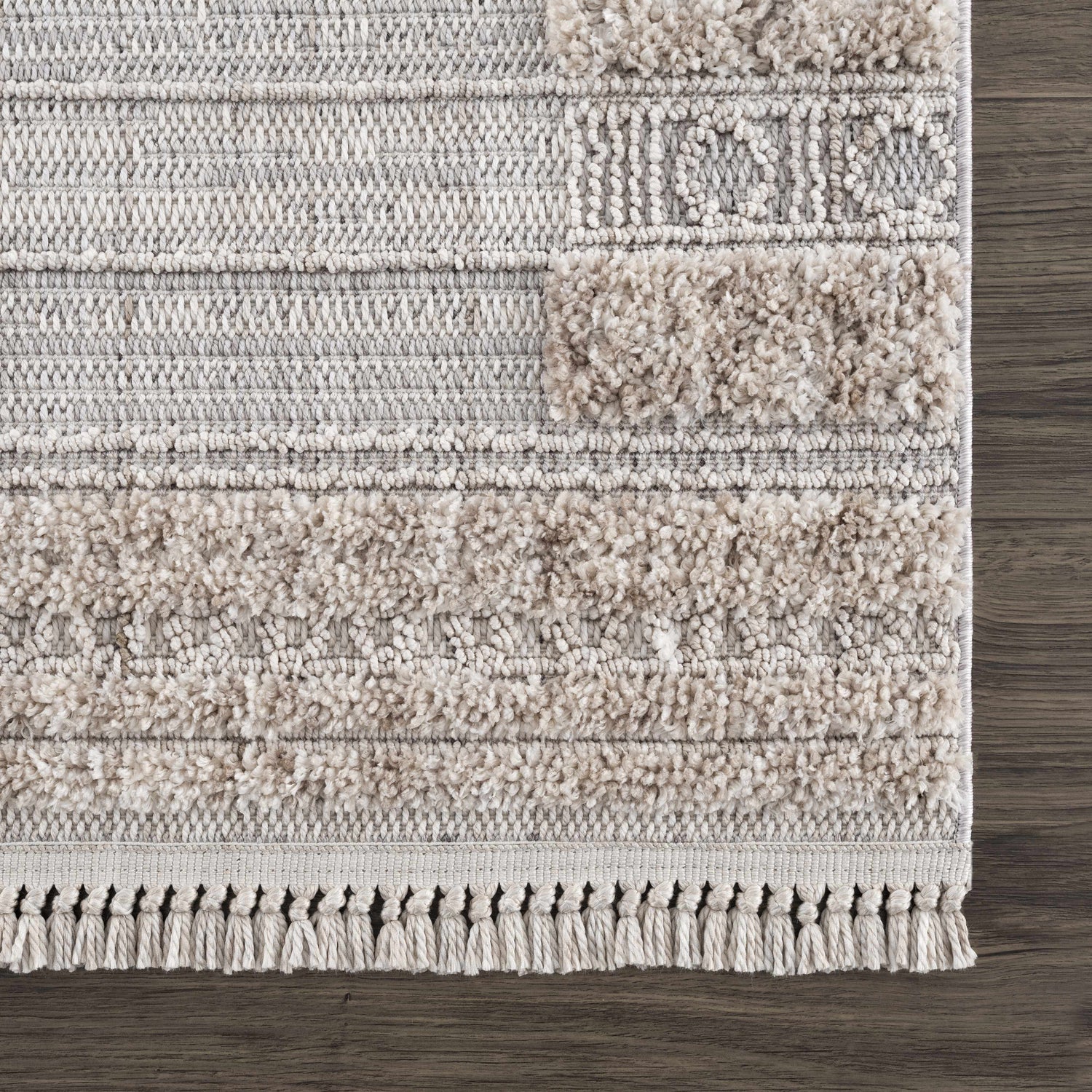 Close up of Sulak Cream Area Rug showing textured, geometric design in cream, beige, and gray on dark wood floor. Swatch