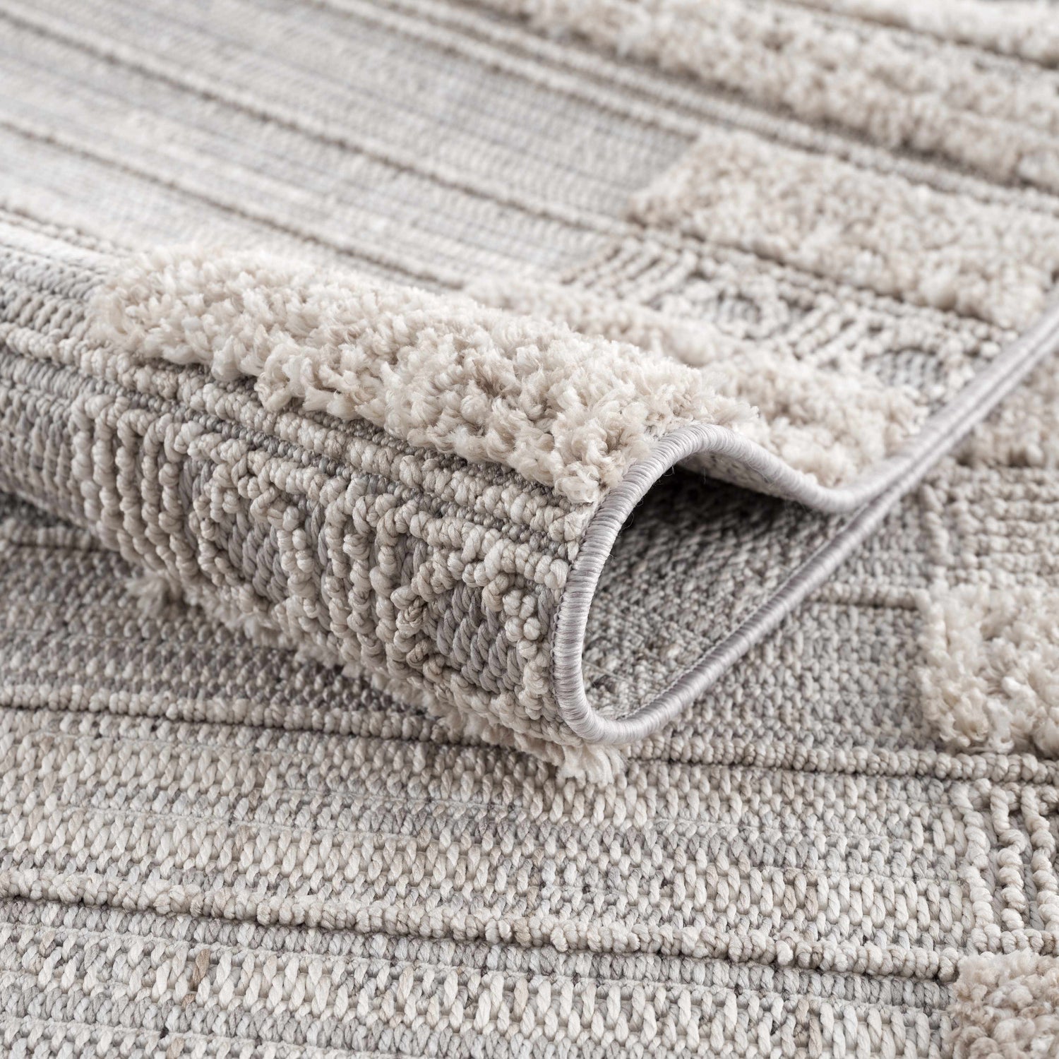 Close-up of the Sulak Cream Area Rug showing the textured, geometric pattern and soft pile. Neutral colors. Fold