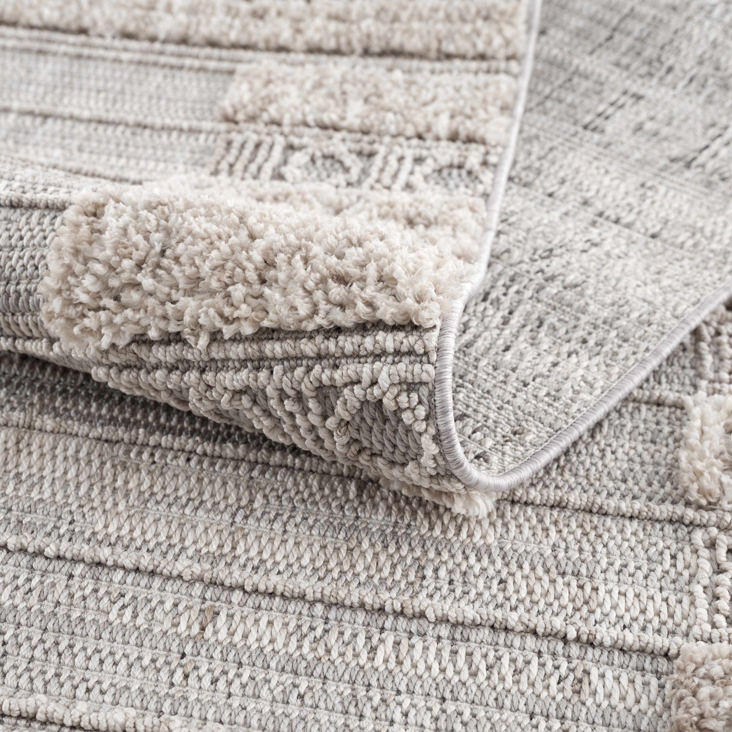 Close-up of Sulak Cream Area Rug showing the textured weave, cream shag accents, and light gray tones. Fold