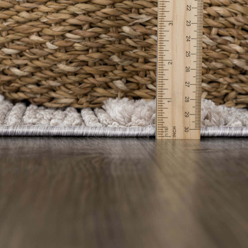 Close-up of the Sulak Cream Area Rug showing its pile height with a ruler and a woven basket in the background. Pile