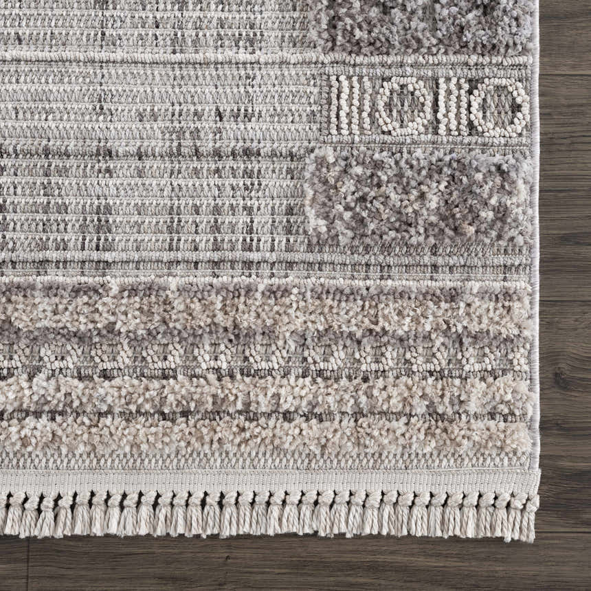 Close-up of the Naivasha Elegant High/Low Area Rug showing its charcoal, cream, and gray textured design and fringe. Swatch