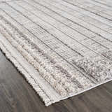 Close-up of the Naivasha Elegant High/Low Area Rug. Cream and charcoal rug with a textured, striped pattern and fringe detail. Corner