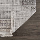 Close-up of Naivasha Elegant High/Low Area Rug showing charcoal, cream, and gray tones, plus fringe detail and rug backing. Fold