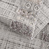 Close-up of the Naivasha Elegant High/Low Area Rug. Features a textured geometric pattern in charcoal, cream, and gray polyester. Fold