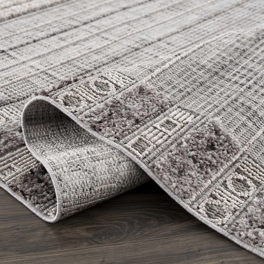 Close-up of the Naivasha Elegant High/Low Area Rug showing its charcoal, cream, and gray textured pattern. Fold