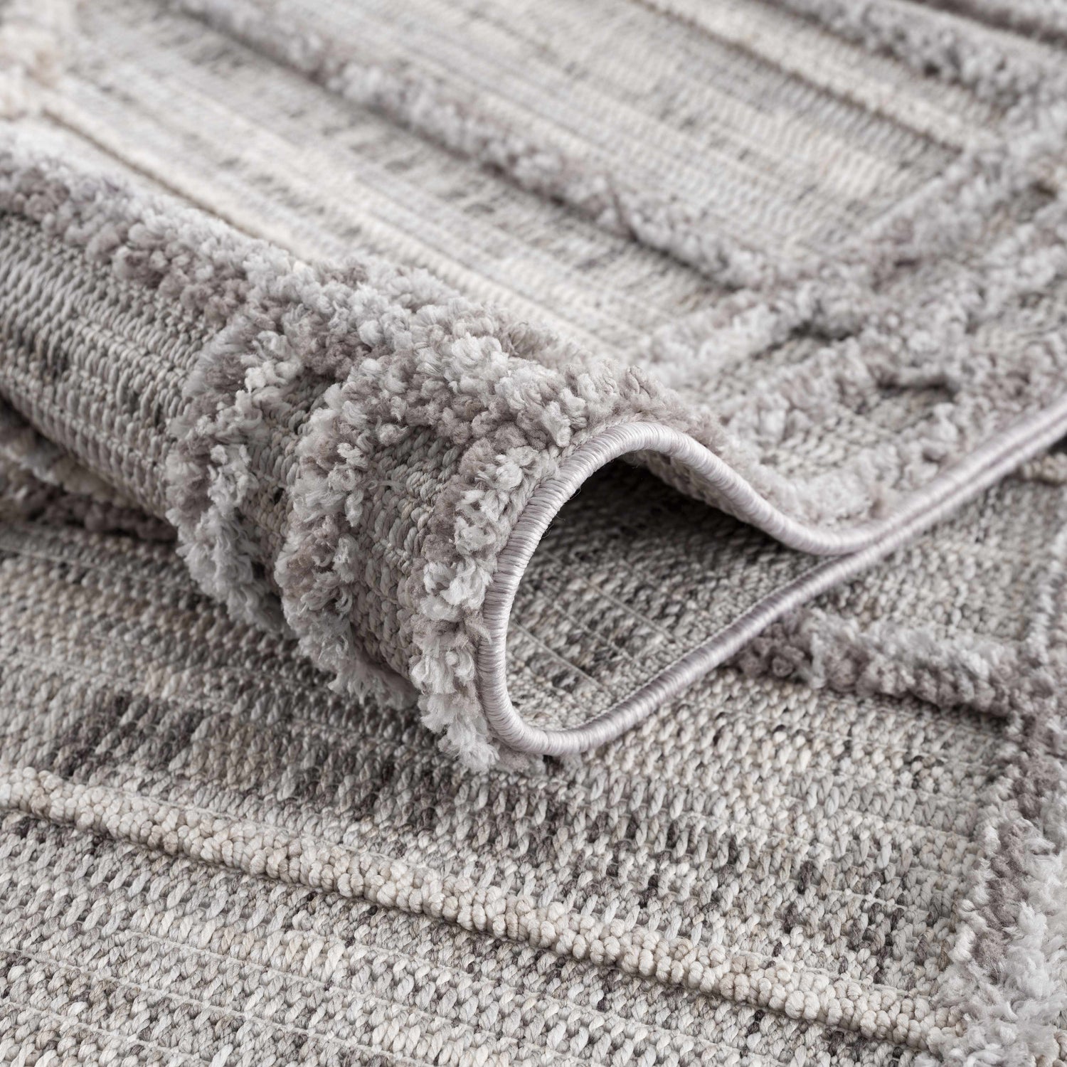Close-up of the Barurao Area Rug showing its charcoal, cream, and gray geometric pattern and soft, textured pile. Fold