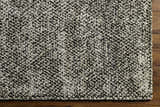 Close-up of the Abiba Area Rug showing its beige and black contemporary design and hand-loomed texture on a wood floor. Corner