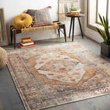 Living room scene with Arncliffe Washable Area Rug in orange, brown, and ivory. Bohemian style with bench, plant, and decorative pillows. Roomscene-Rectangle