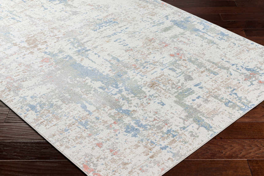Close-up of the Ahava Washable Area Rug. Abstract pattern in white, blue, gray, and tan on dark wood floors. Corner