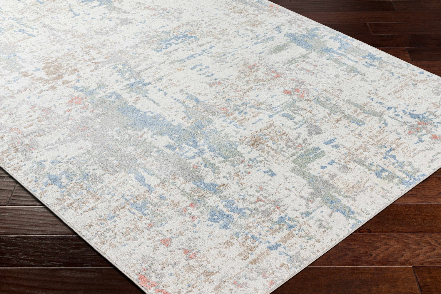 Close-up of the Ahava Washable Area Rug. Abstract pattern in white, blue, gray, and tan on dark wood floors. Corner