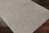 Close-up of the hand-loomed Ahmeek Area Rug in medium gray viscose, featuring a subtle striped texture on a dark wood floor. Corner