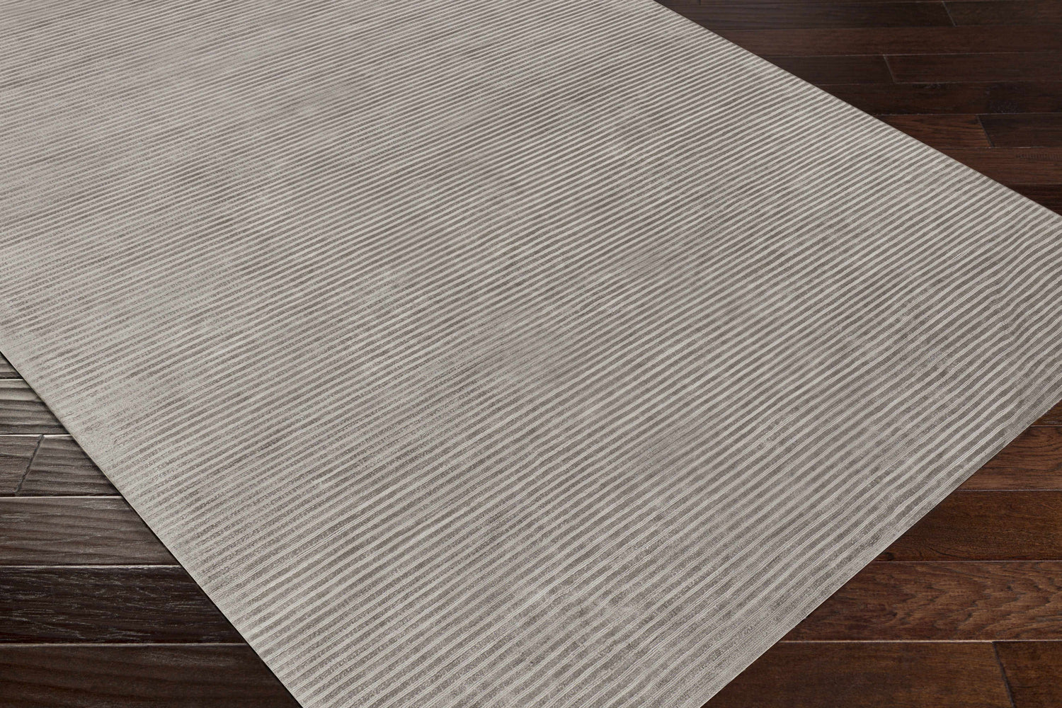 Close-up of the hand-loomed Ahmeek Area Rug in medium gray viscose, featuring a subtle striped texture on a dark wood floor. Corner