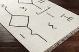 Close-up of the AISHA Area Rug, a hand-woven runner with a geometric black pattern on a cream wool and viscose blend. Corner