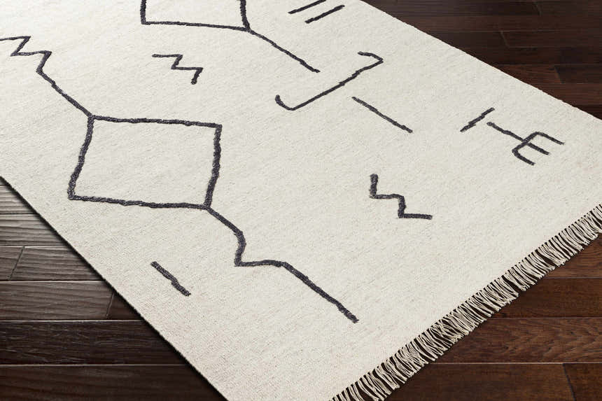 Close-up of the AISHA Area Rug, a hand-woven runner with a geometric black pattern on a cream wool and viscose blend. Corner