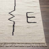 Close-up of the hand-woven AISHA Area Rug. Beige wool rug with a black geometric pattern and fringe. Contemporary style. Front