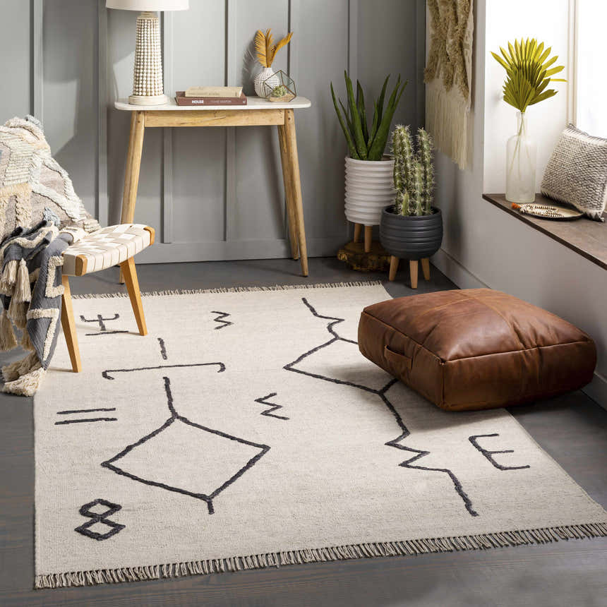 Living room scene with Aisha area rug, geometric pattern, neutral tones, leather pouf, and modern decor. Roomscene-Rectangle