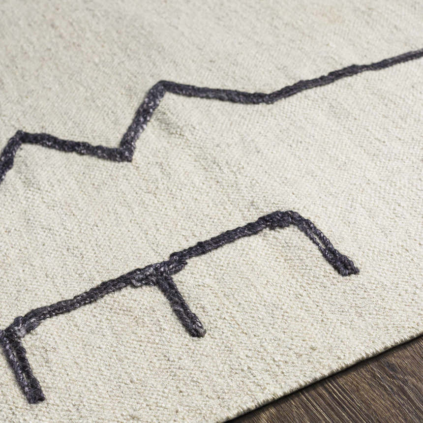 Close up of the Aisha Area Rug showing its ivory wool texture and geometric charcoal design. Texture