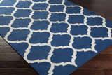 Close-up of the Alcalde Area Carpet on dark wood floors. Features a bright blue and ivory quatrefoil pattern. Hand woven cotton rug. Corner