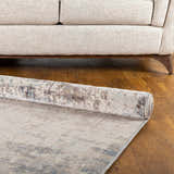 Rolled Alcove Abstract Area Rug in dark blue, gray, and ivory on a wood floor with a beige sofa. Fold