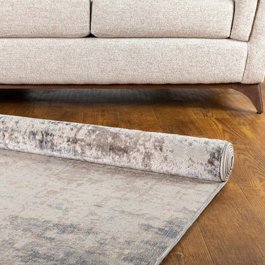 Rolled Alcove Abstract Area Rug in dark blue, gray, and ivory on a wood floor with a beige sofa. Fold