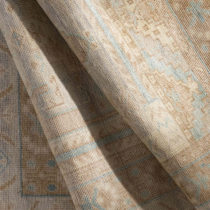 Close-up of the hand-knotted Aliang Premium Rug. Tan, cream, and light blue colors with a traditional oriental pattern. Wool texture. Fold