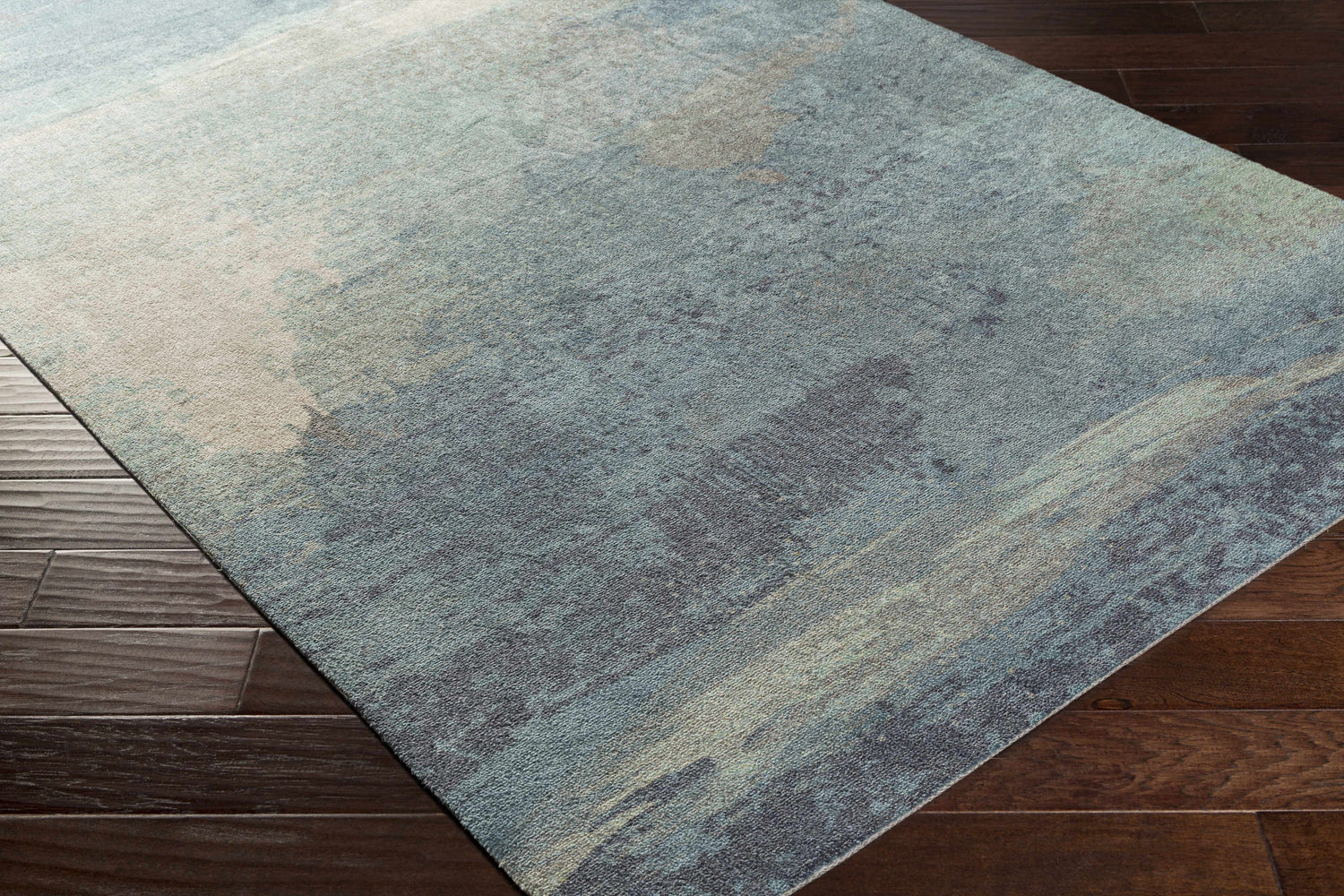 Close-up of the Alvaton Abstract Blue Rug showing its denim, gray, and light blue abstract design on dark wood floors. Corner