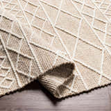 Close-up of the Ambulong Area Rug, a hand-woven rug with a cream and tan geometric pattern and medium brown wool and cotton texture. Fold