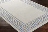 Close-up of Alen Cream & Blue Indoor Outdoor Rug showing Greek key border pattern and textured weave on dark wood floor. Corner