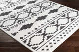 Close-up of the Amoret Area Rug, a machine-woven rug with a black and off-white geometric pattern on dark wood floors. Corner