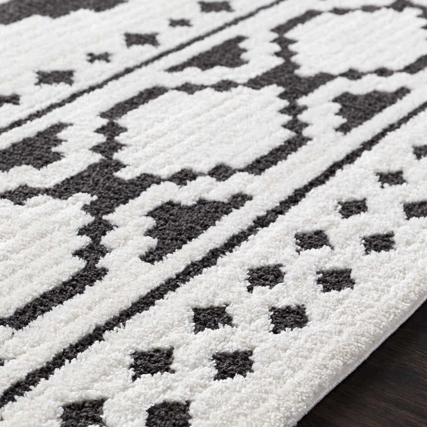 Close up of the Amoret Area Rug showing its black and off-white bohemian pattern and textured weave. Texture