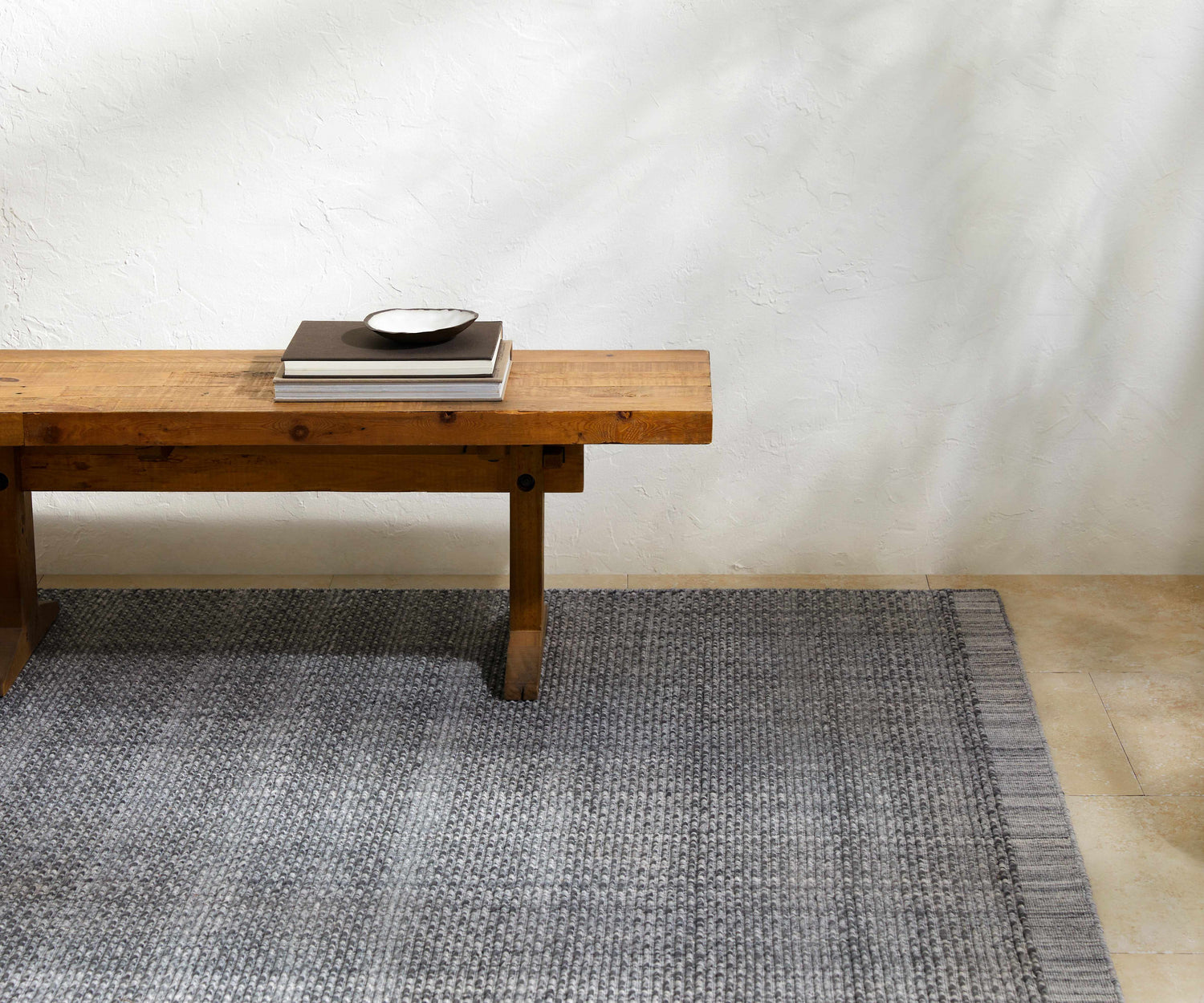 Minimalist entryway with a Yong Hand Loomed Gray rug, wooden bench, and textured white wall. Styleshot
