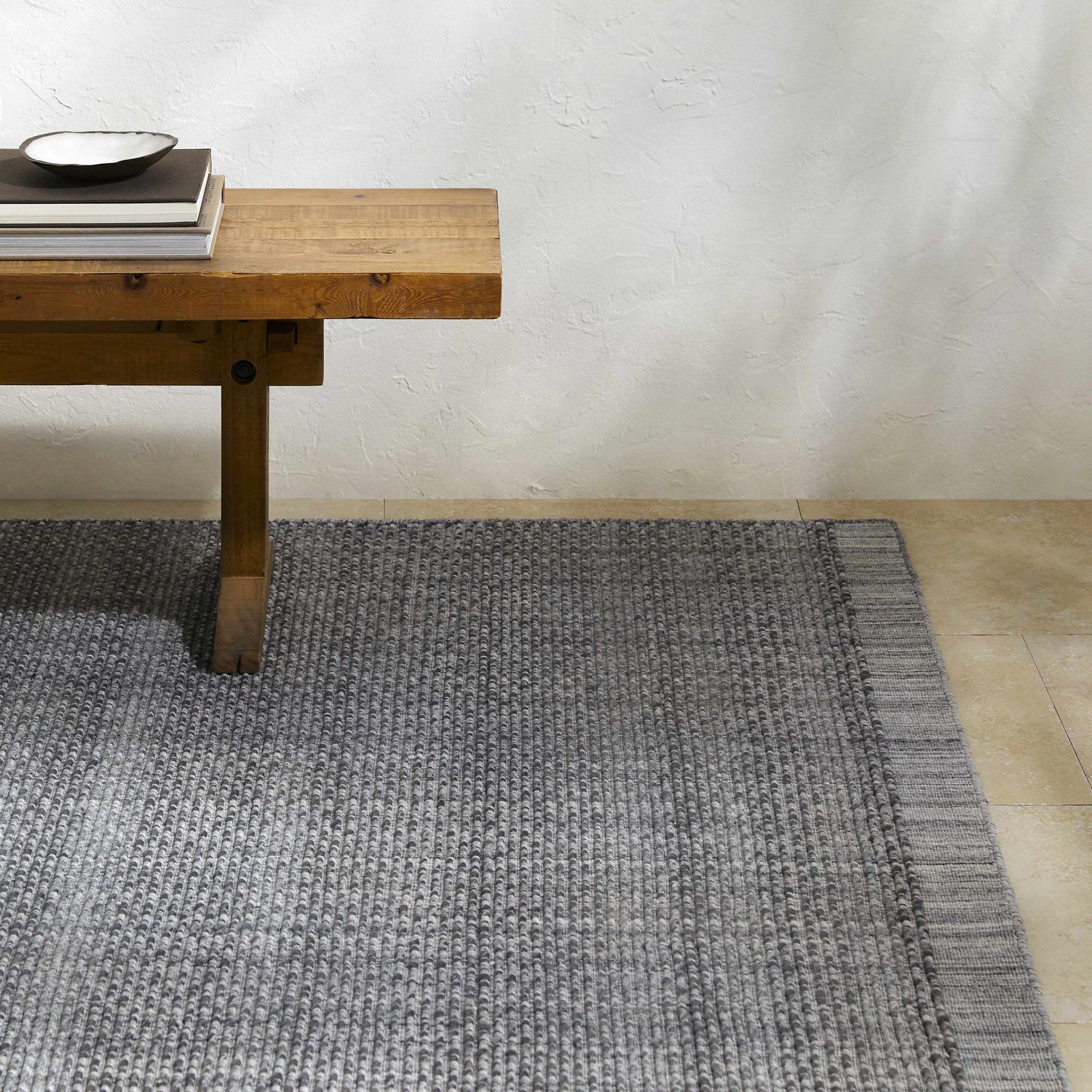 Entryway scene with Yong Hand Loomed Gray Indoor Outdoor Rug and wood bench with books. Styleshot
