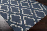 Close-up of the Anchorage Area Carpet, a hand-woven wool rug in cream and dark blue with a geometric pattern. Corner