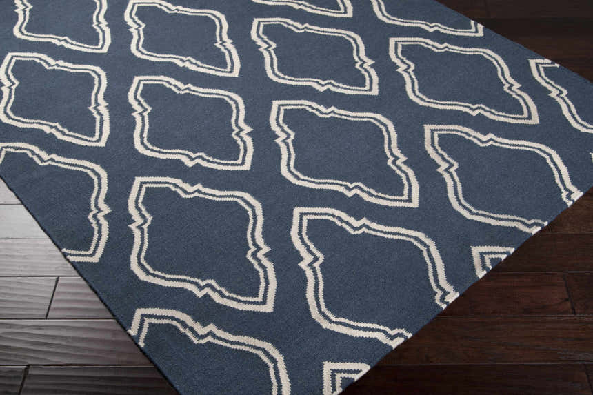 Close-up of the Anchorage Area Carpet, a hand-woven wool rug in cream and dark blue with a geometric pattern. Corner
