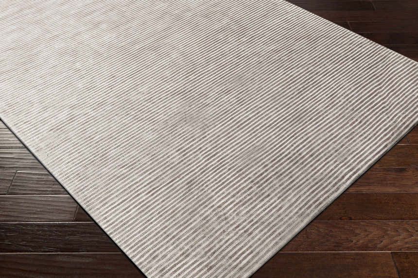 Close up of the Angie Area Rug in charcoal, featuring a contemporary striped design and viscose texture on dark wood floors. Corner