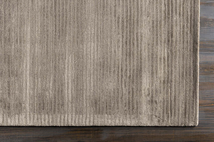 Close-up of the charcoal Angie Area Rug showing its hand-loomed, striped texture on dark wood flooring. Corner