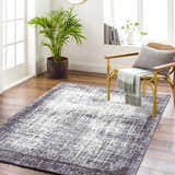 Living room scene with Binh Gray Area Rug, wood floors, straw chair, and potted plant creating a cozy, contemporary vibe. Roomscene-Rectangle