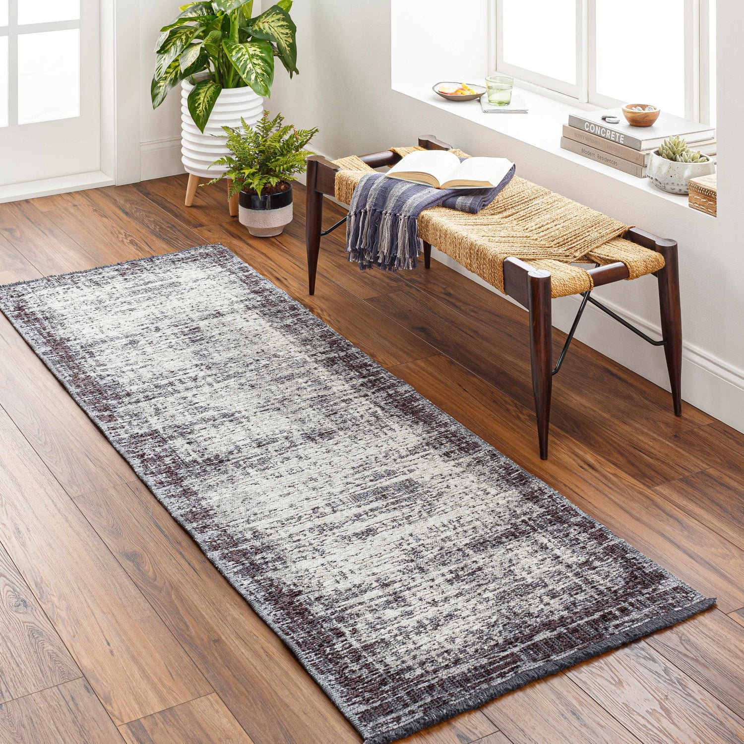 Entryway with Binh Gray Area Rug runner, wood floors, and a woven bench with open book near a window. Roomscene-Runner