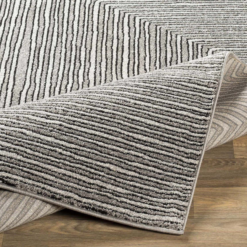 Close-up of the Artois Area Rug showing its black, cream, and gray striped pattern and textured jute and polypropylene material. Fold