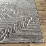 Close-up of the Artois Area Rug showing a geometric pattern in black, cream, gray, and slate on a wood floor. Front