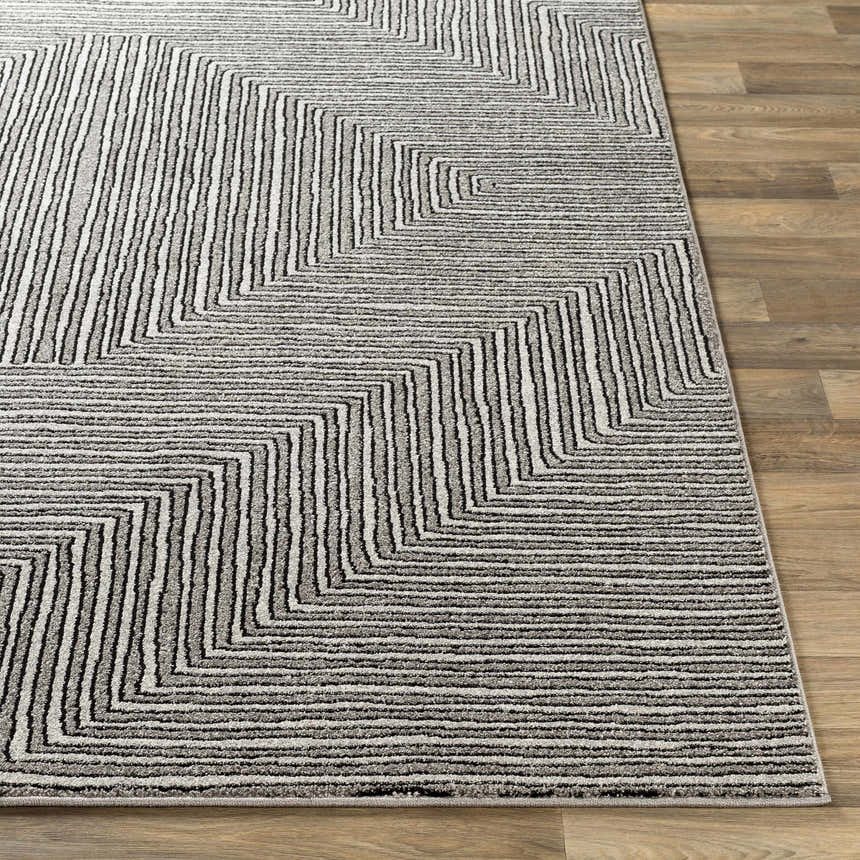 Close-up of the Artois Area Rug showing a geometric pattern in black, cream, gray, and slate on a wood floor. Front