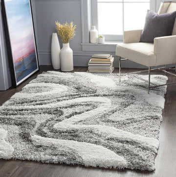 Living room scene with gray walls, off-white chair, and Asfordby Gray Canyon Plush Rug in charcoal, gray, and off-white. Roomscene-Rectangle